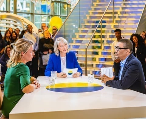 3 presenters at a table with the public around them